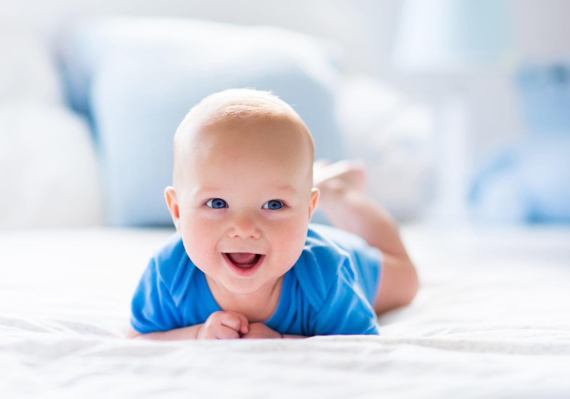 Adorable baby boy in white sunny bedroom. Newborn child relaxing in bed. Nursery for young children. Textile and bedding for kids. Family morning at home. New born kid during tummy time with toy bear.